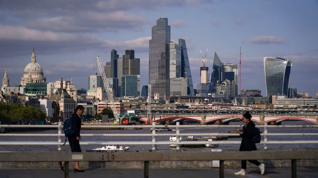 Commuters walk along Waterloo Bridge, against the backdrop of the skyline of the financial district of the City of London, Monday, June 5, 2023. (AP Photo/Alberto Pezzali)